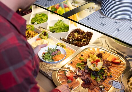 A man picks salad and meat from a buffet.