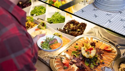 Ein Mann wählt Salat und Fleisch von einem Buffet.