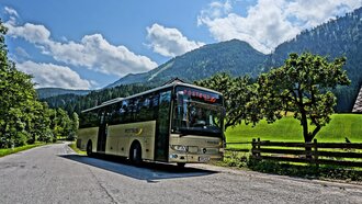 A Postbus stops in a picturesque mountain setting with trees.