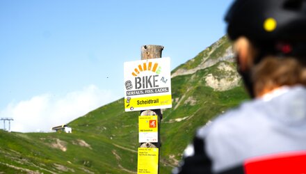 Sign for the Scheidtrail bike route in Serfaus, surrounded by mountains.