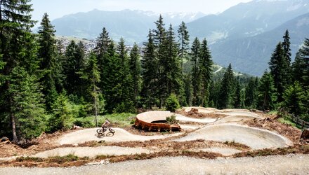 Biker auf einem Trails im Wald mit Alpenblick.