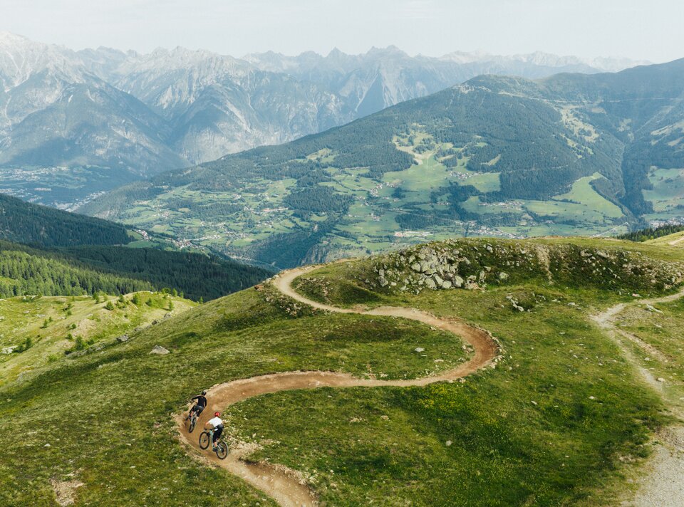 Two mountain bikers ride a winding path in the mountains.