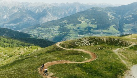 Zwei Mountainbiker fahren einen kurvenreichen Pfad in den Bergen.