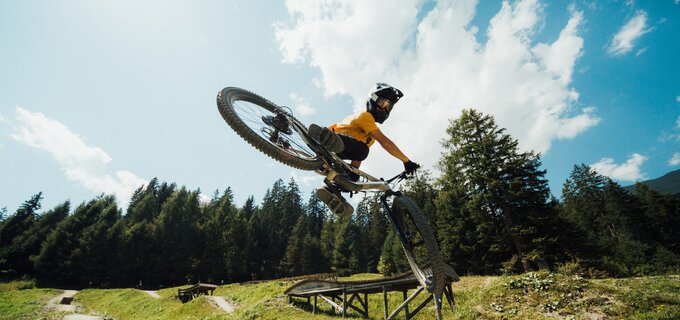 Ein Biker springt mit einem Mountainbike über eine Rampe im Wald.