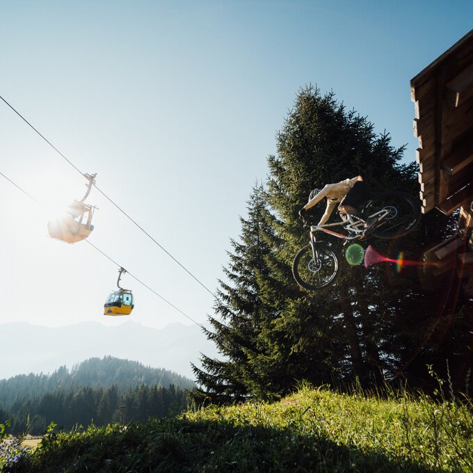 Ein Mountainbiker spritzt während eines Sprungs vor einer Lodge.
