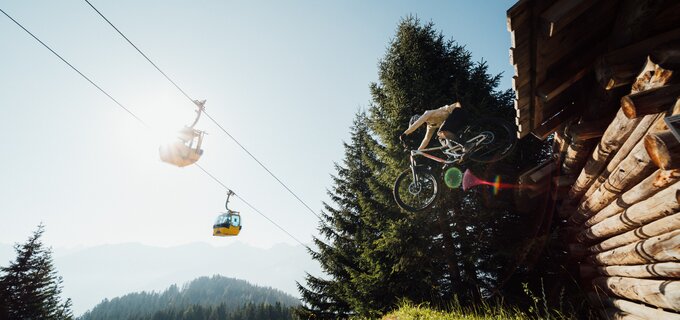Ein Mountainbiker spritzt während eines Sprungs vor einer Lodge.