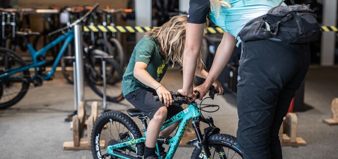 Ein Kind sitzt auf einem Fahrrad, während eine Frau hilft.