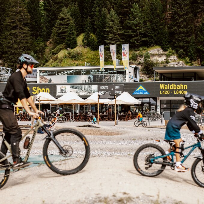 Zwei Mountainbiker fahren in einem Bikepark mit Bergblick.