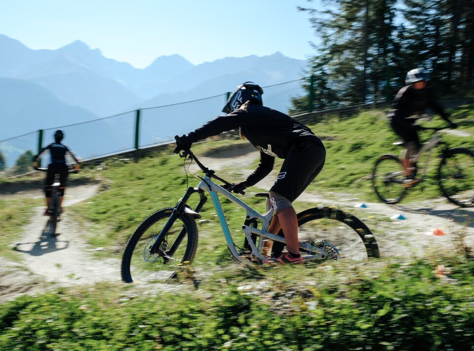 Drei Mountainbiker fahren auf einer kurvigen Strecke in den Bergen.