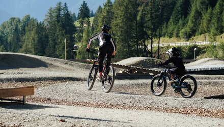 Two mountain bikers riding on a dirt park in sunny weather.