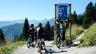 Three mountain bikers stop at the Milky Way sign.