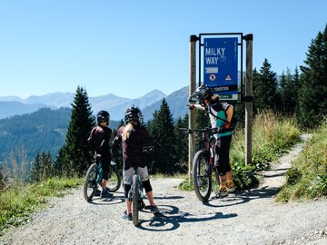 Three mountain bikers stop at the Milky Way sign.