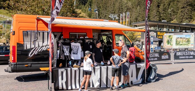 Stand with merchandise at bike festival; visitors checking items.