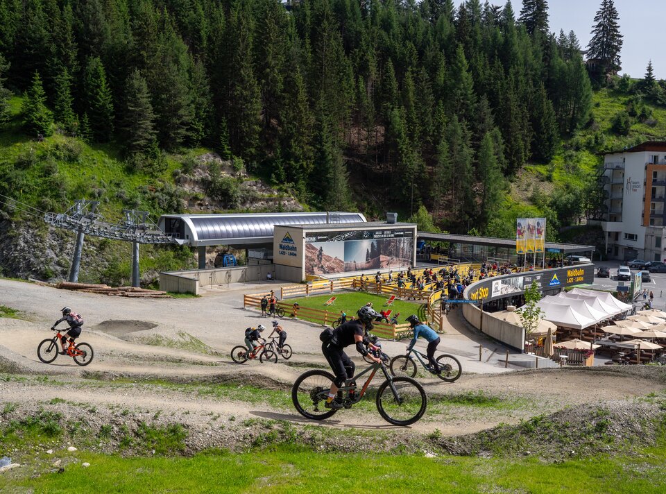 Mountainbiker fahren nahe einer Liftstation in einer grünen Landschaft.