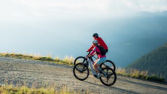Zwei Mountainbiker fahren auf einem schmalen Pfad in den Bergen.
