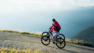 Two mountain bikers riding on a narrow path in the mountains.