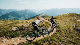Two mountain bikers ride a narrow path in the high mountains.