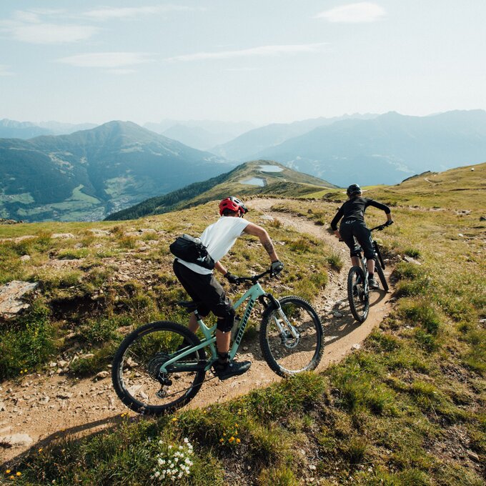 Two mountain bikers ride a narrow path in the high mountains.
