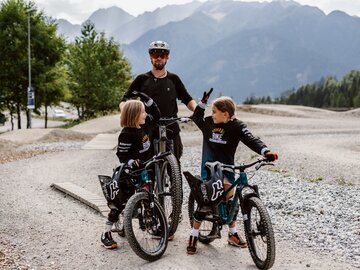 Familie mit Mountainbikes in der Natur, Berge im Hintergrund.