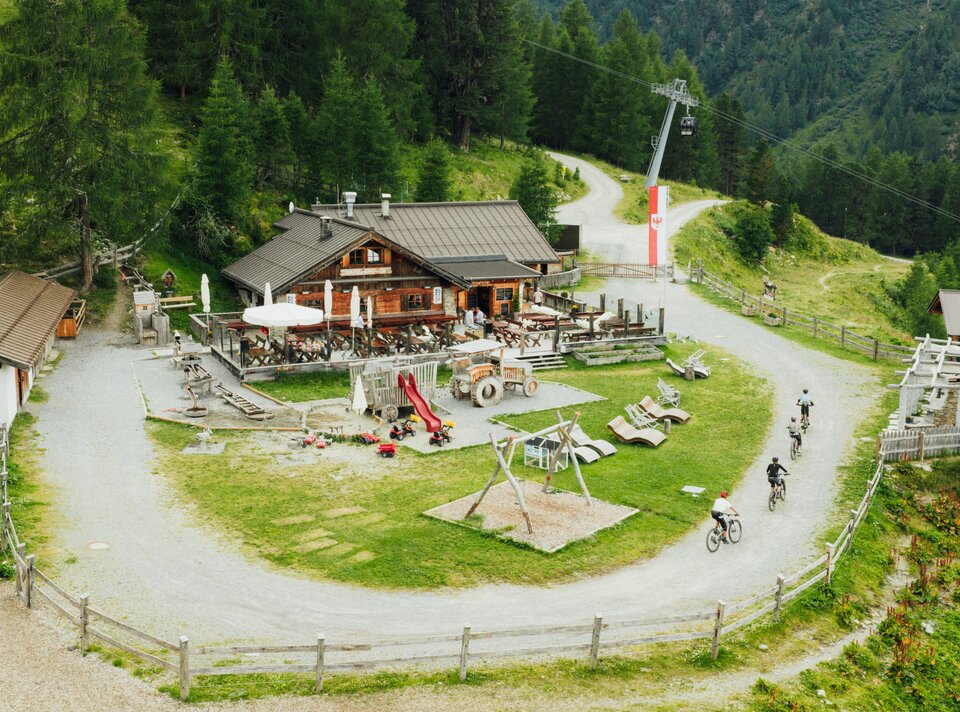 Blick auf eine Berghütte mit Spielplatz, Spielgeräten und Fahrrädern.