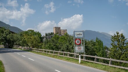 Straßenansicht von Ladis mit einem Verkehrsschild und Burg im Hintergrund.