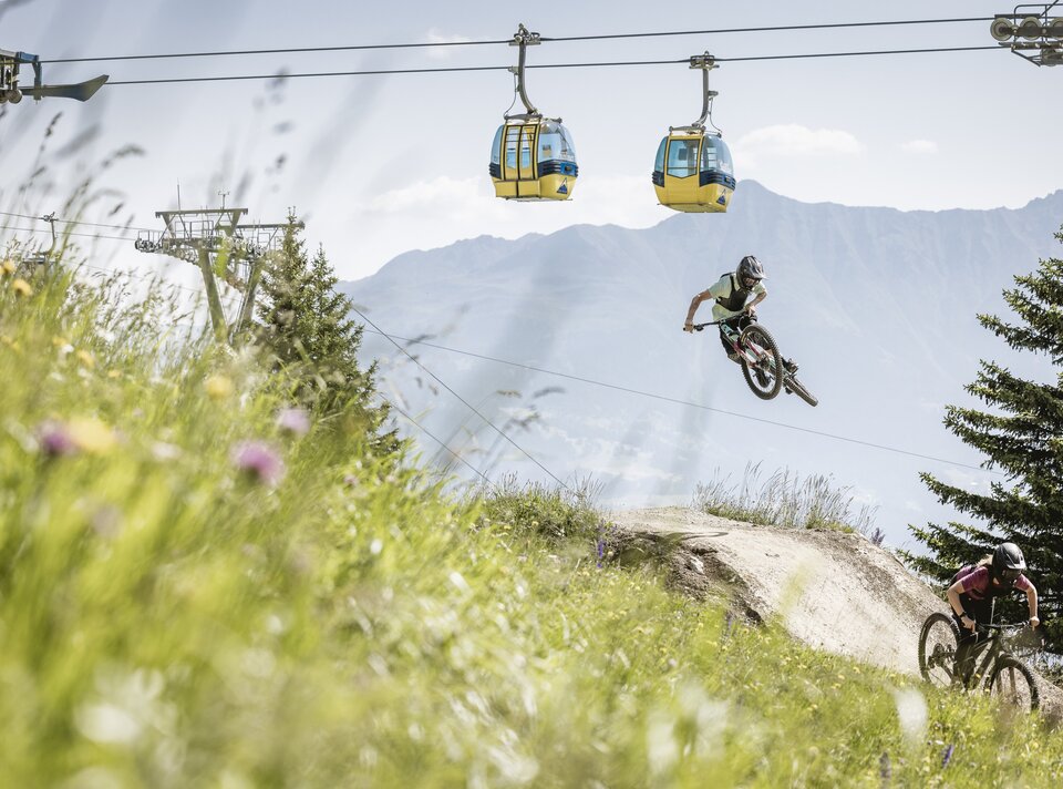 A mountain biker jumps on a track with gondolas above.